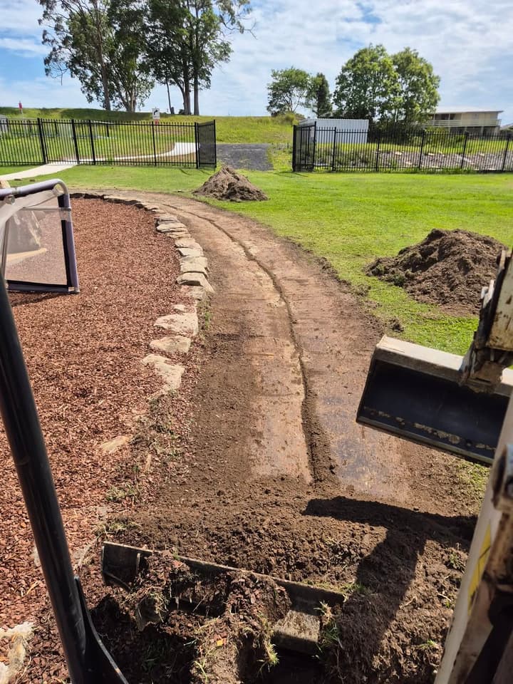 Tight-access excavation alongside a Coffs Harbour building for O'Brien Plumbing & Relining — exposing pipework.